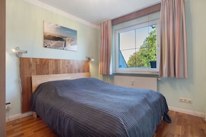 Un dormitorio con cabecera de madera, cama con colcha a rayas, ventana con cortinas e imagen colgada en la pared.