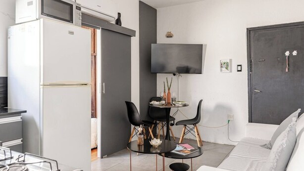 A compact living space with a kitchenette, a dining area with two chairs, a flat-screen TV mounted on the wall, and a sofa. - Parque Rodó | Private terrace | BBQ (Montevideo)