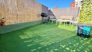 A backyard with artificial grass, a barbecue grill, outdoor furniture, and a bamboo fence. - Parque Rodó | Private terrace | BBQ (Montevideo)