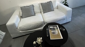 A modern living room with a white sofa, two grey cushions, a black coffee table with a remote control and a magazine, and a small potted plant. - Parque Rodó | Private terrace | BBQ (Montevideo)