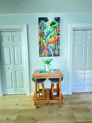 A room with a wooden table and two chairs, a colorful abstract painting on the wall, and white doors.