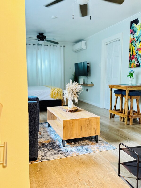 A modern living room with a wooden coffee table, a sofa, a TV mounted on the wall, and a ceiling fan.