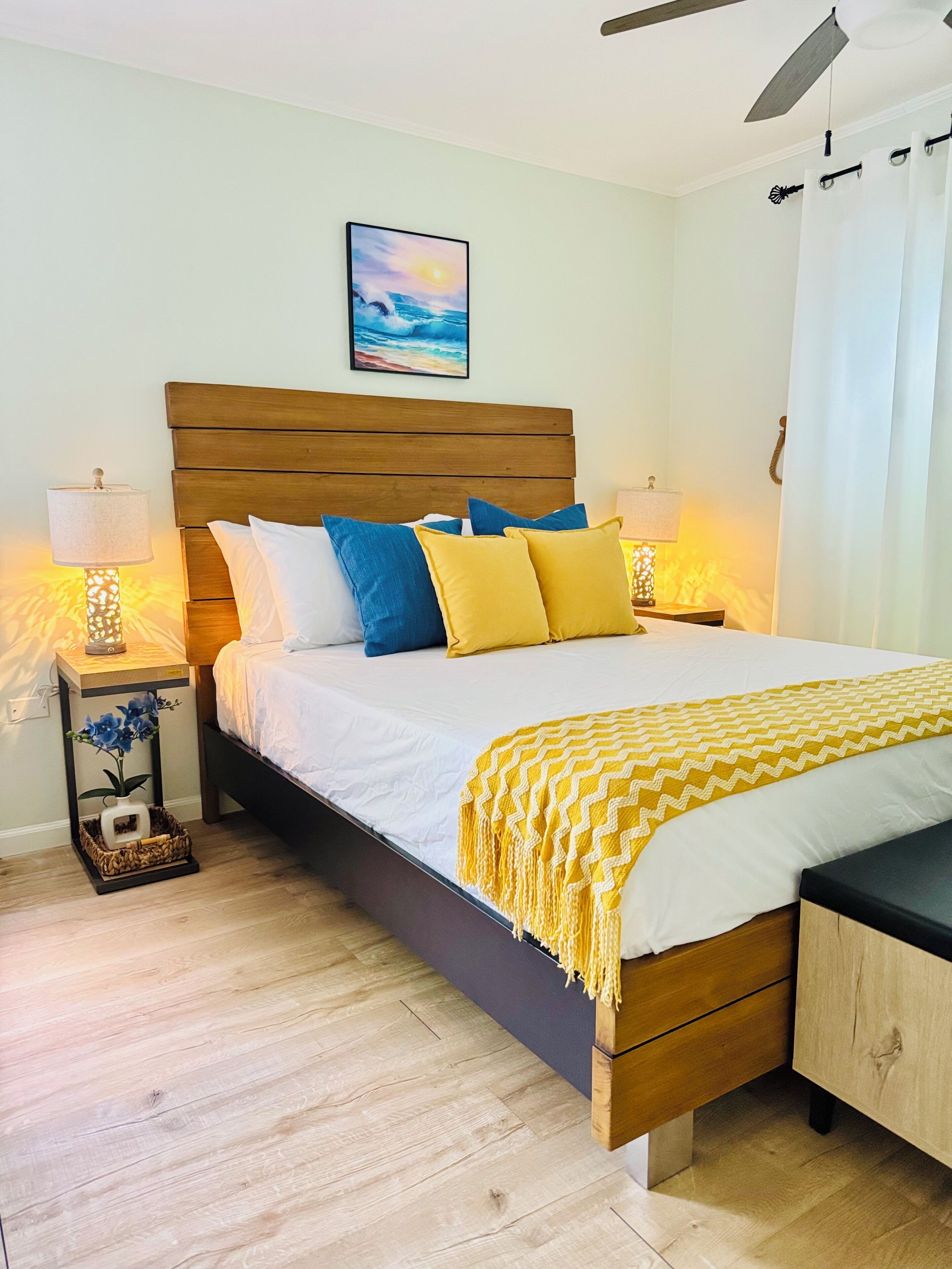 A neatly arranged bedroom with a wooden bed, two bedside tables with lamps, a wall-mounted picture, and a ceiling fan.