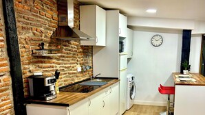 Una cocina moderna con pared de ladrillo, encimera de madera, armarios blancos y lavadora integrada.