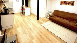 Amplia sala de estar con piso de madera, un sofá marrón, una zona de cocina con estufa y armarios, y una mesa de comedor con sillas.