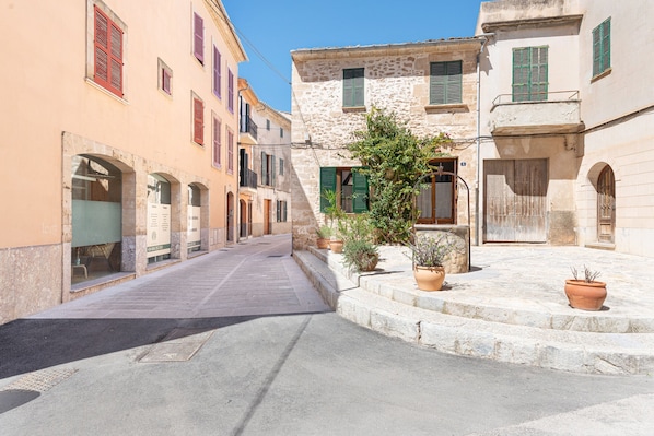 A narrow street with buildings on either side, stone steps, and potted plants.