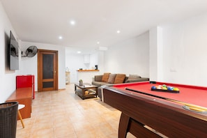 A living room with a pool table, a sofa, a red table, and a television.