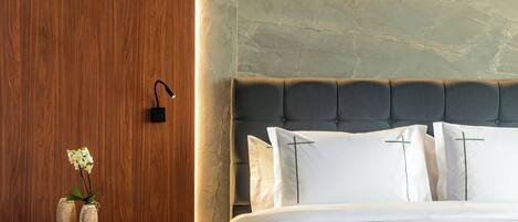 A modern bedroom with a wooden wall, a bedside table with a vase and a basket, a bed with white bedding and a grey headboard, and a grey sofa.
