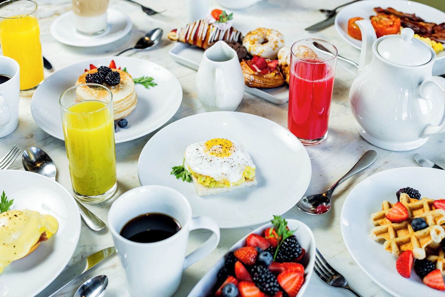 Un desayuno con diferentes opciones de comida, como panqueques, gofres y un sándwich, acompañado de bebidas y salsas.