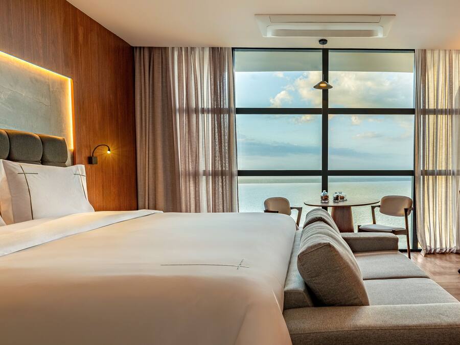 Ett hotellrum med en stor säng, en soffa, ett matbord och utsikt över havet.