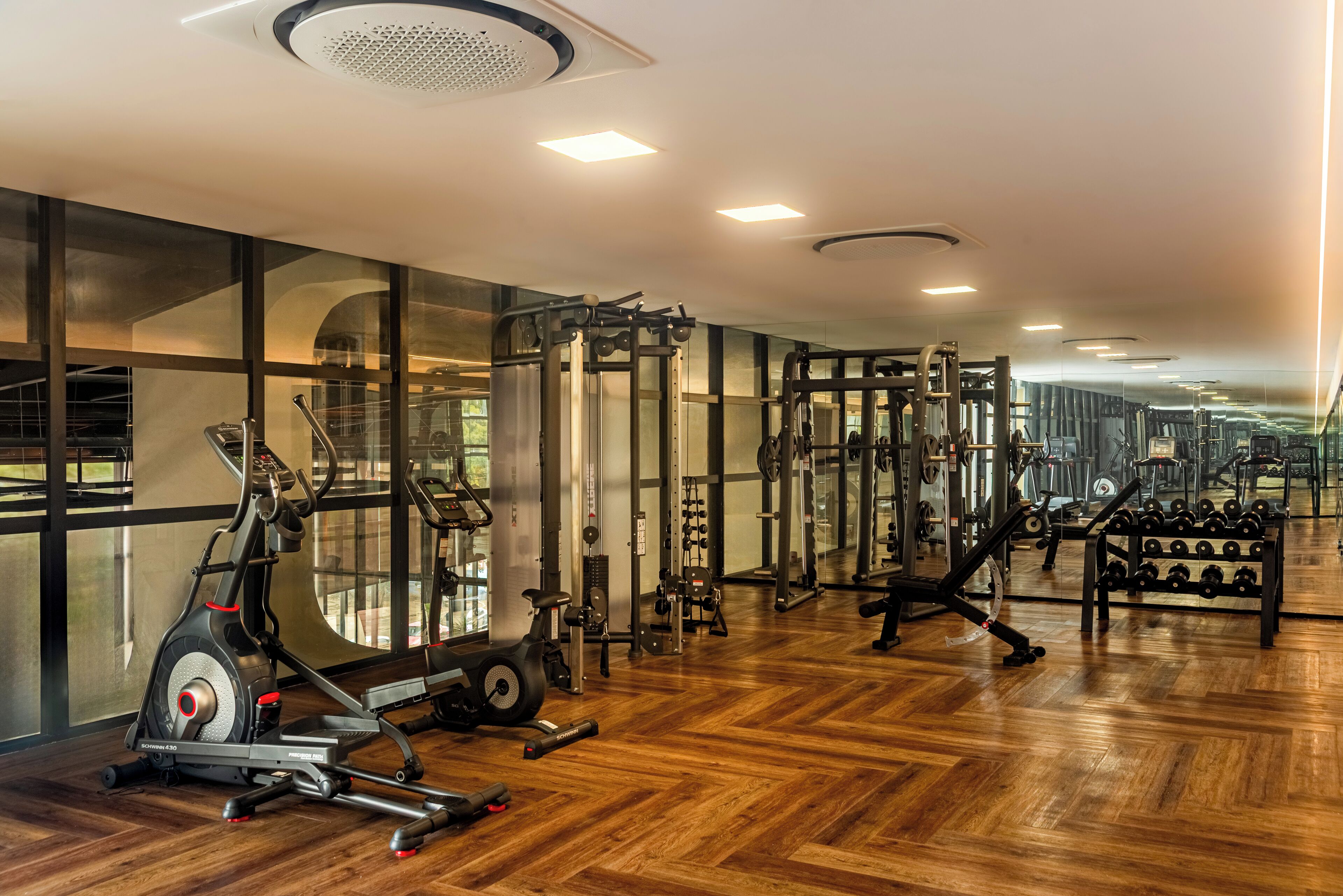 A gym with exercise equipment, wooden flooring, and large windows.