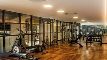 A gym with exercise equipment, wooden flooring, and large windows.