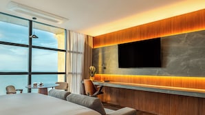 Una camera d'albergo moderna con un letto grande, un'area salotto con un tavolo e una TV montata su una parete in legno.