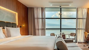 Camera d'hotel con un letto grande, un divano, un tavolo da pranzo e vista sul mare.