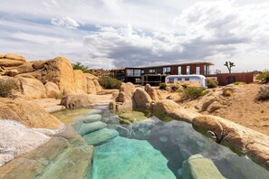 A modern house with a swimming pool surrounded by natural rock formations. - Iconic 7,000sf Glass Villa w/ 2 Pools on 350 Acres (Pioneertown)