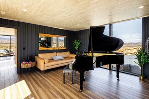 Ein modernes Wohnzimmer mit einem Klavier, einem Sofa und einem großen Fenster mit Blick auf eine Wüste.