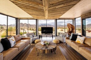 A spacious living room with leather sofas, a central coffee table, and a large TV. - Iconic 7,000sf Glass Villa w/ 2 Pools on 350 Acres (Pioneertown)