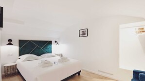A modern hotel room with a large bed, a headboard with a geometric pattern, a small round side table, a wall-mounted picture, and a window with curtains. - Luxurious Apartment - 3br/6p - Nation (Paris)