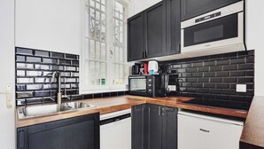 A modern kitchen with black cabinets, a dishwasher, a microwave, and a coffee maker. - Luxurious Apartment - 3br/6p - Nation (Paris)