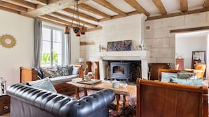 A living room with a fireplace, wooden beams, a sofa, a table, and a patterned rug.