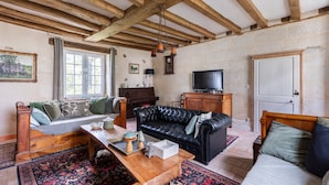 A living room with a wooden ceiling, a sofa, a television, and a piano.