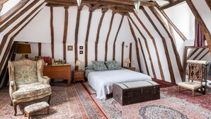 Une chambre avec un plafond en pente, un lit, une chaise, une table de chevet, une lampe, une petite table, un banc et un tapis.