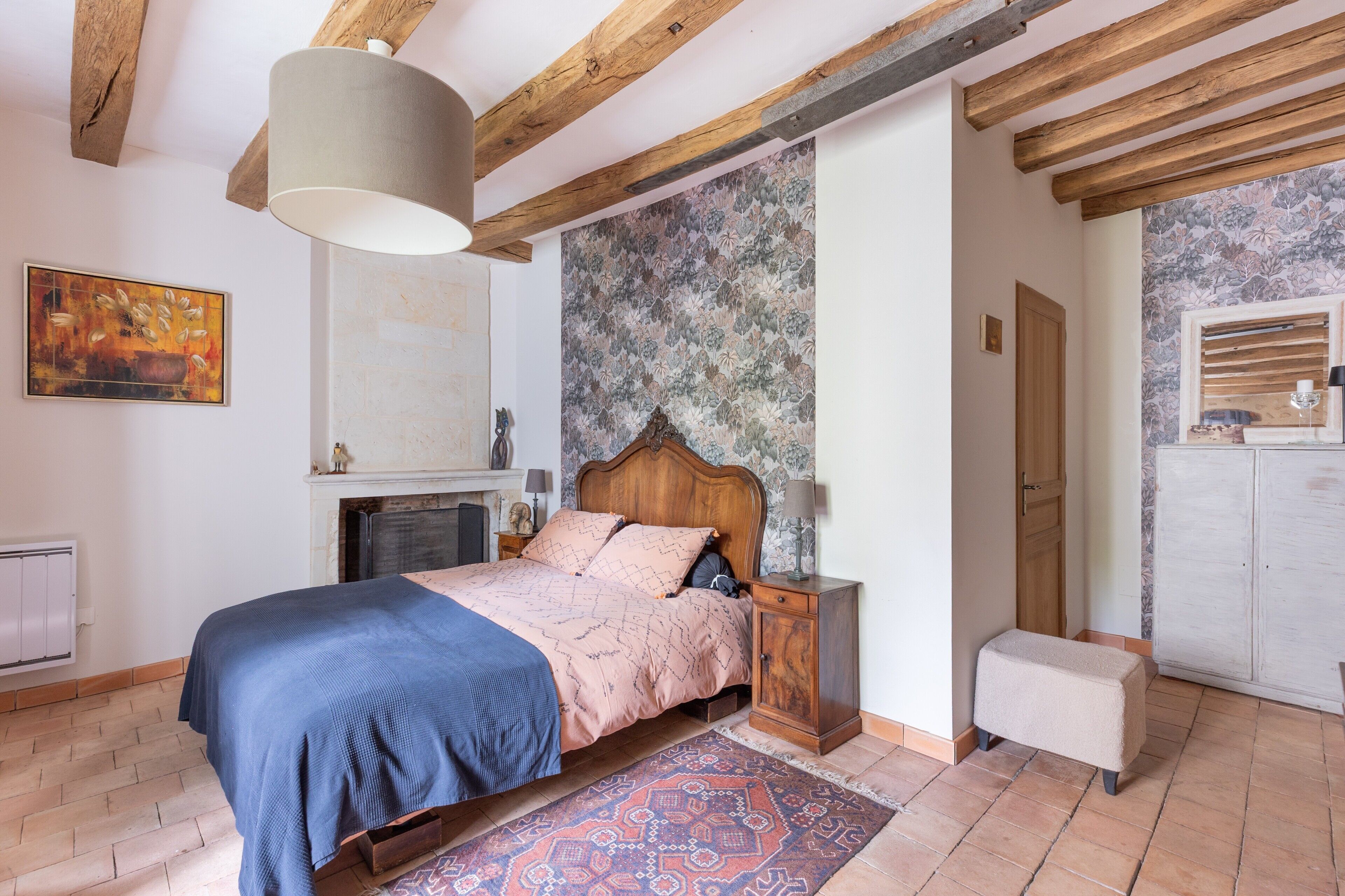 A bedroom with a bed, nightstand, bench, and a fireplace.