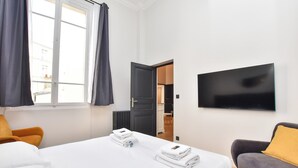 A hotel room with a bed, a TV, a sofa, and a window with curtains. - Charming Apartment - 2br/7p - Arc de Triomphe (Paris)