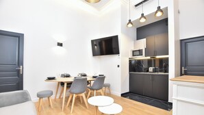 A modern kitchen with a flat-screen TV, wooden cabinets, and a dining area with a table and chairs. - Charming Apartment - 2br/7p - Arc de Triomphe (Paris)