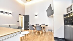 A modern living room with a sofa, dining table, and chairs. There is a TV mounted on the wall and a kitchen area with a microwave. - Charming Apartment - 2br/7p - Arc de Triomphe (Paris)