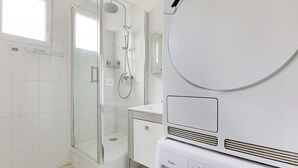 Un baño moderno con ducha acristalada, lavabo blanco y una lavadora Whirlpool.