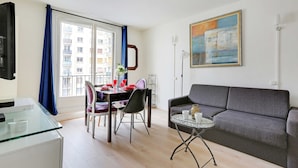Una sala de estar moderna con un sofá gris, una mesa de comedor con sillas rojas y una mesa de centro de vidrio.