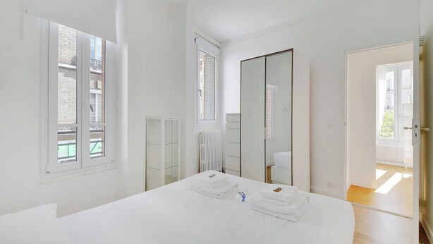 A bedroom with a large bed, a wardrobe, a radiator, and a window with blinds. - Cozy Apartment 2bdr/5p - in the Heart of Suresnes (Suresnes)