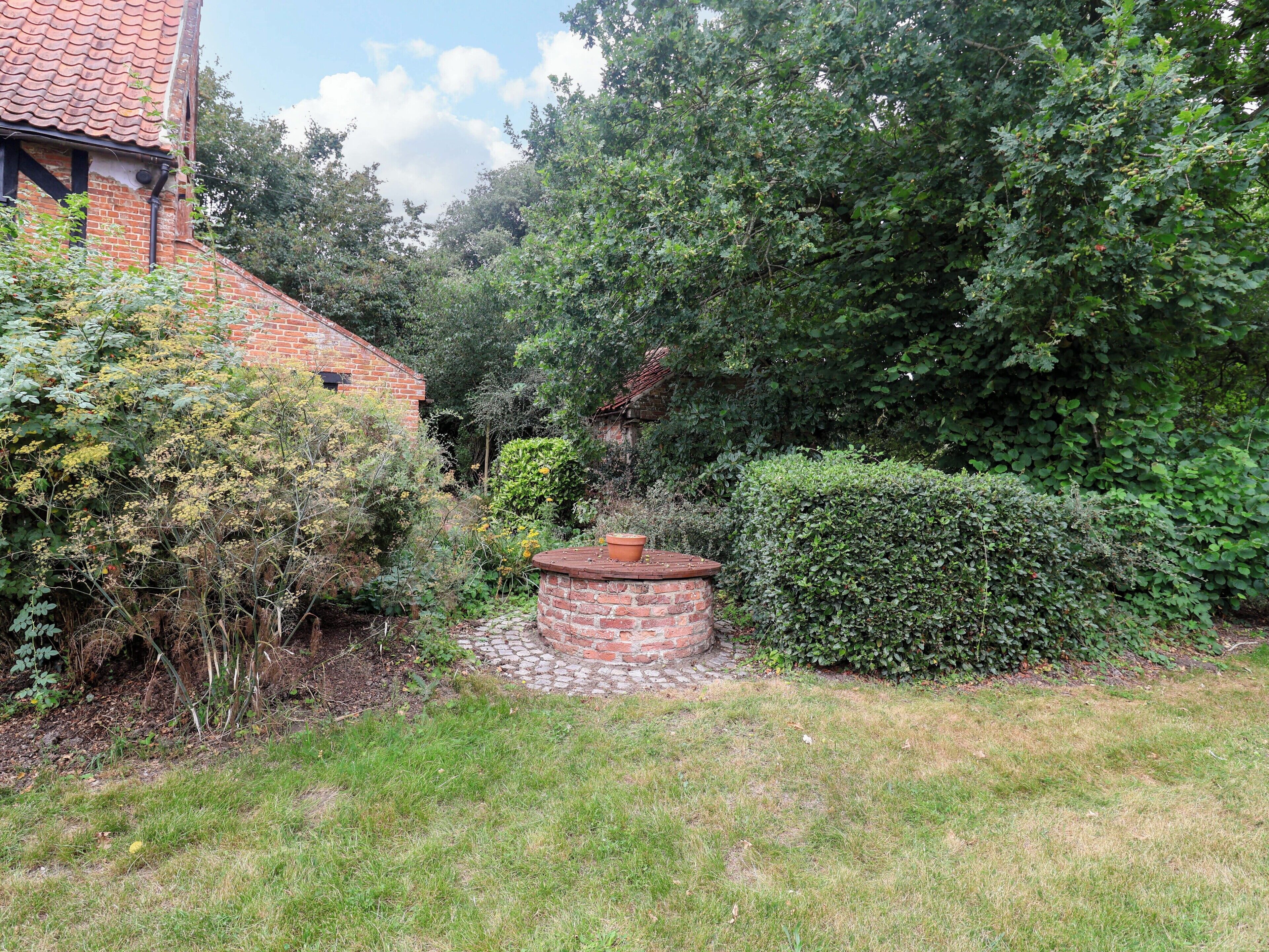 Een bakstenen huis met een pannendak, omgeven door weelderige begroeiing en een verzorgde tuin.