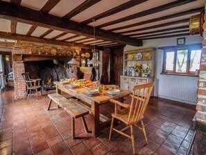 A rustic dining area with exposed wooden beams, a brick fireplace, and a wooden bench. - Keirs Cottage (Beccles)