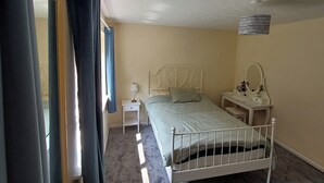 Una camera da letto con un letto singolo, un comodino con una lampada, uno specchio e una piccola mensola.