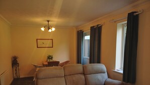 Un soggiorno con divano, un lampadario, un quadro incorniciato, un tavolino con una pianta e una finestra con tende.