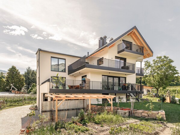 Une maison moderne à deux étages, dotée d’un balcon, d’une pergola et d’un jardin.