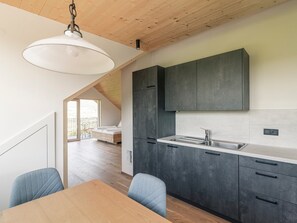 Une cuisine moderne avec des meubles de couleur sombre, un plafond en bois et un coin repas comprenant une table et des chaises.