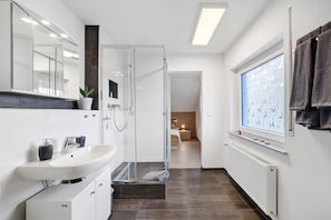 A modern bathroom with a glass shower, white sink, and a large window with a view.