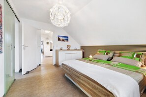 Ein Schlafzimmer mit einem hölzernen Bett, einem weißen Nachttisch, einer blumigen Pendelleuchte und Blick auf eine Stadtansicht durch das Fenster.