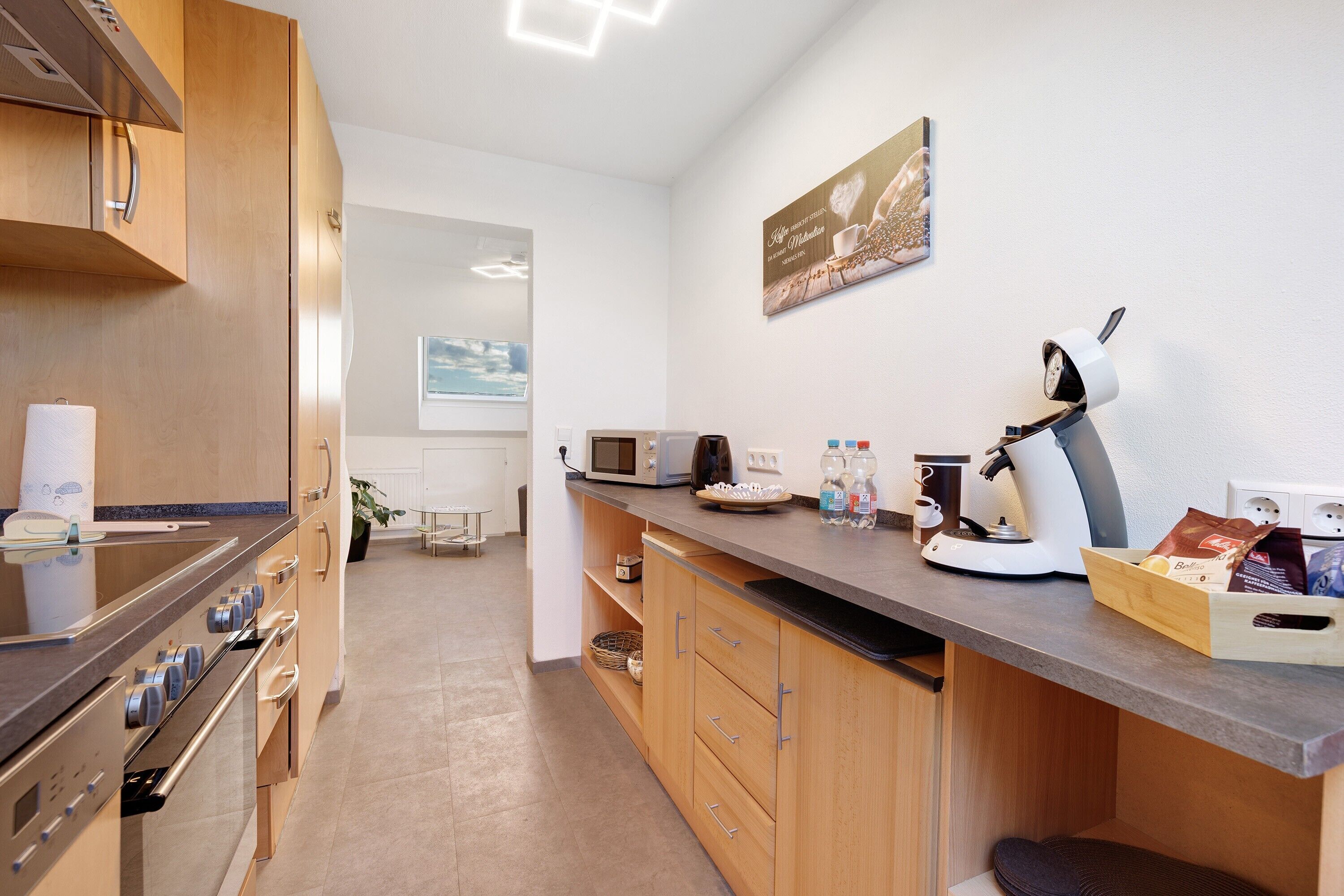 A modern kitchen with stainless steel appliances, wooden cabinets, and a countertop with a coffee machine and coffee cups.