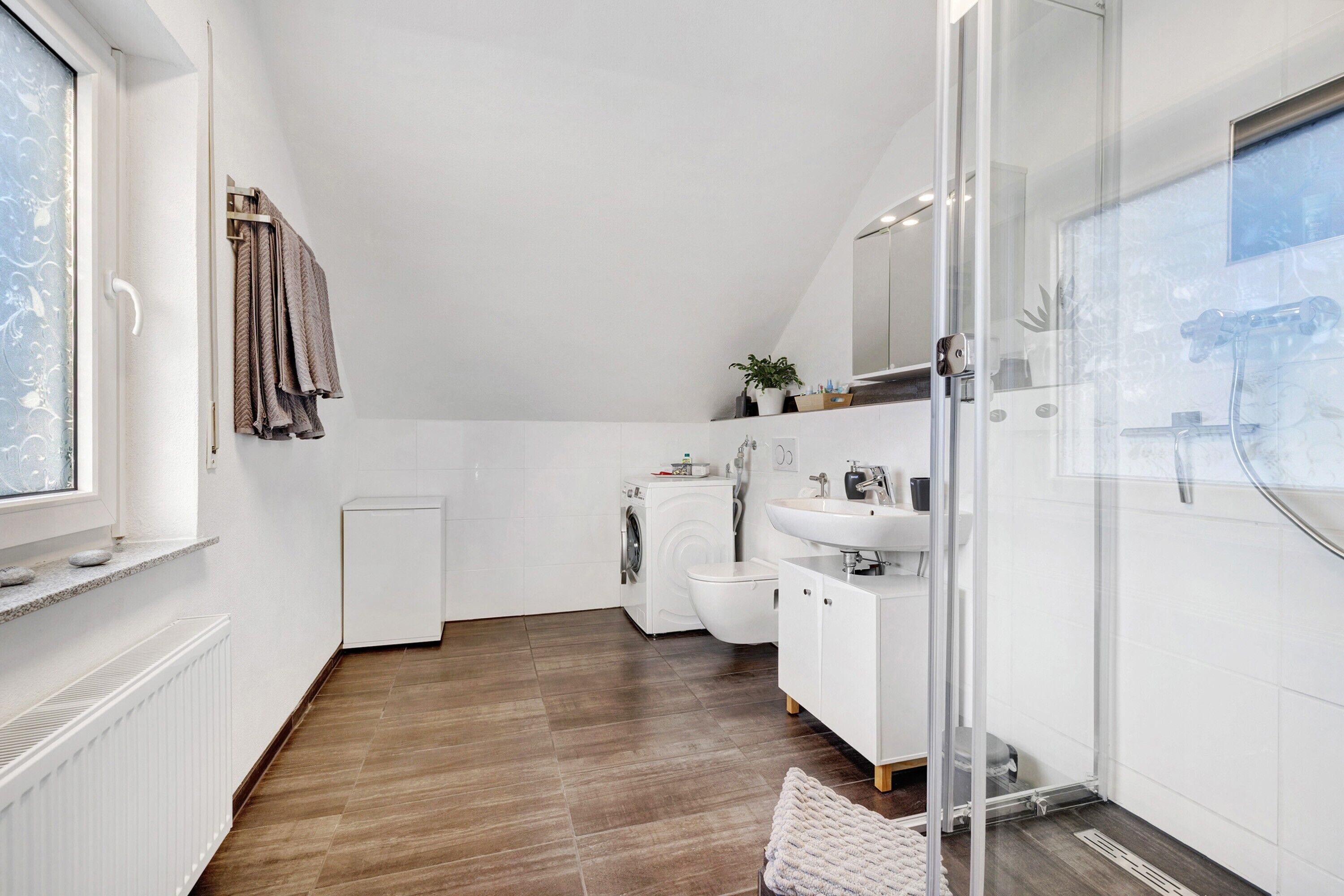 Ein modernes Badezimmer mit Dusche, Toilette und Waschbecken, einem Fenster und einem Handtuchhalter.