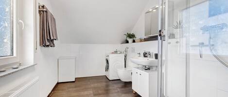 Ein modernes Badezimmer mit Dusche, Toilette und Waschbecken, einem Fenster und einem Handtuchhalter.