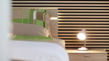 A neatly made bed with a green and white patterned bedspread, a bedside lamp, and a wooden nightstand with a drawer.