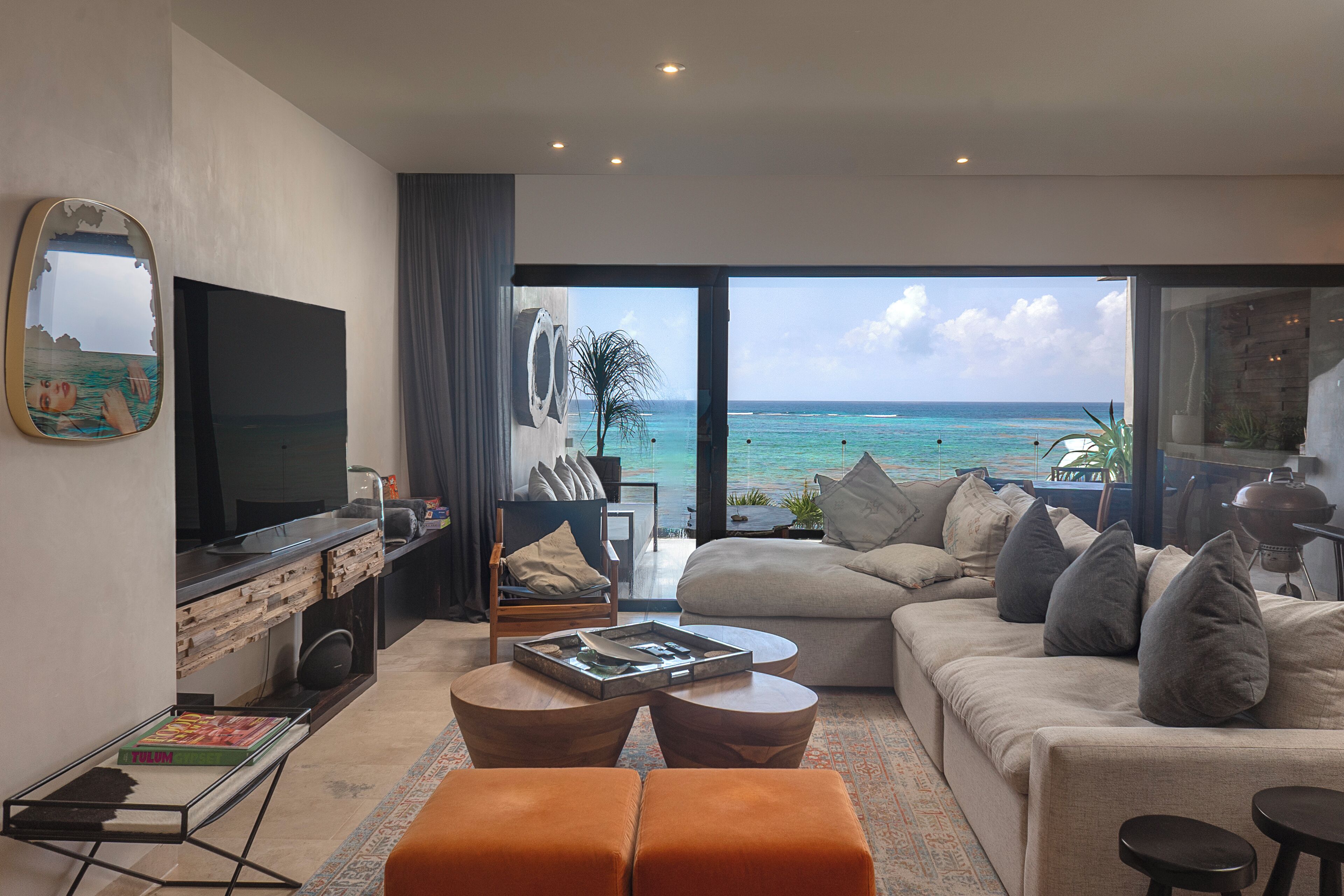 A modern living room with a large TV, comfortable seating, and a view of the ocean.