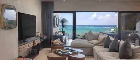 A modern living room with a large TV, comfortable seating, and a view of the ocean.