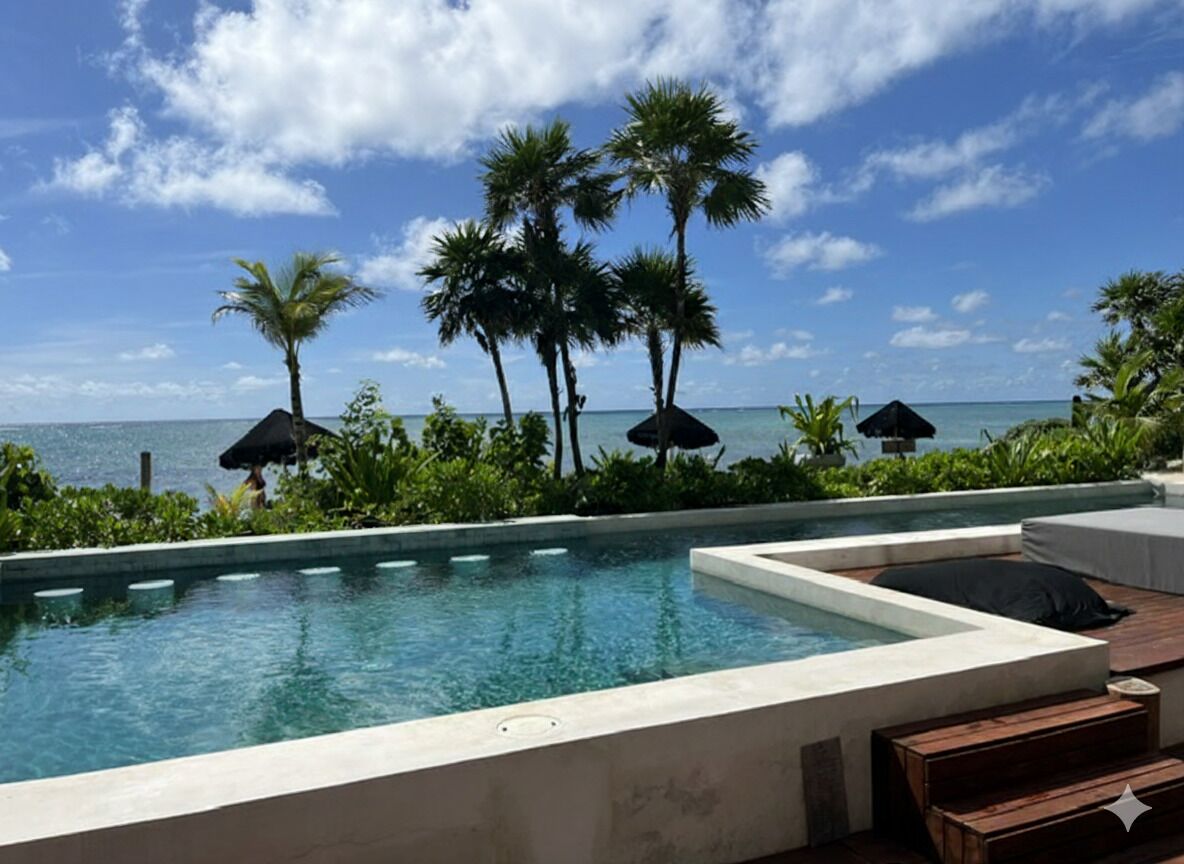 A pool area with a view of the ocean, surrounded by palm trees and umbrellas.