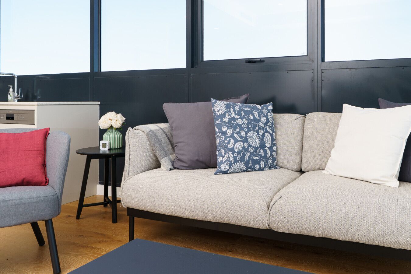 A modern living room with a grey sofa, a red chair, and a small side table with a vase of flowers.