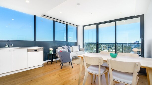 A modern kitchen with white cabinets and a dishwasher, a dining area with a table and chairs, and large windows offering a view of the city. - Bright 1BR Apartment with Stunning Views (Turner)